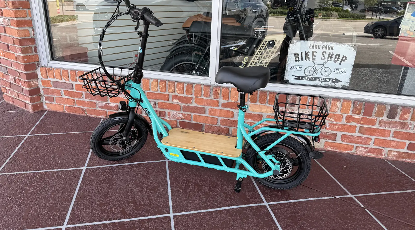 A teal seated electric scooter parked outside Lake Park Bicycles in North Palm Beach